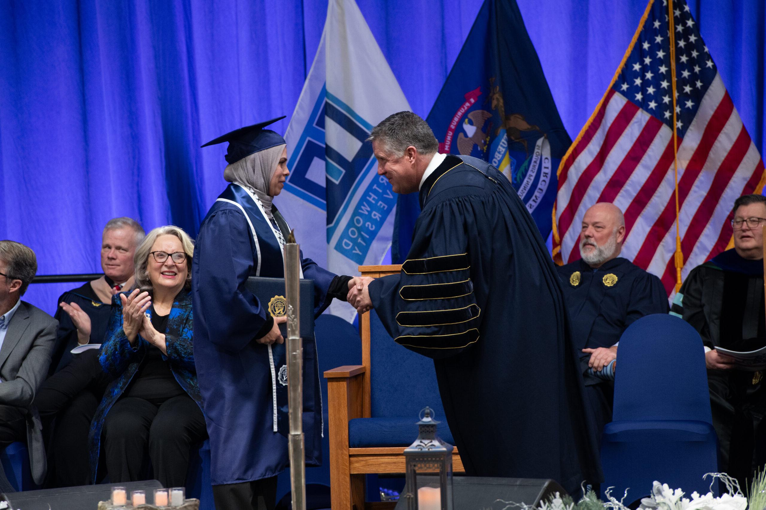 竞技宝app下载 graduate on stage shaking hands with the President after accepting diploma