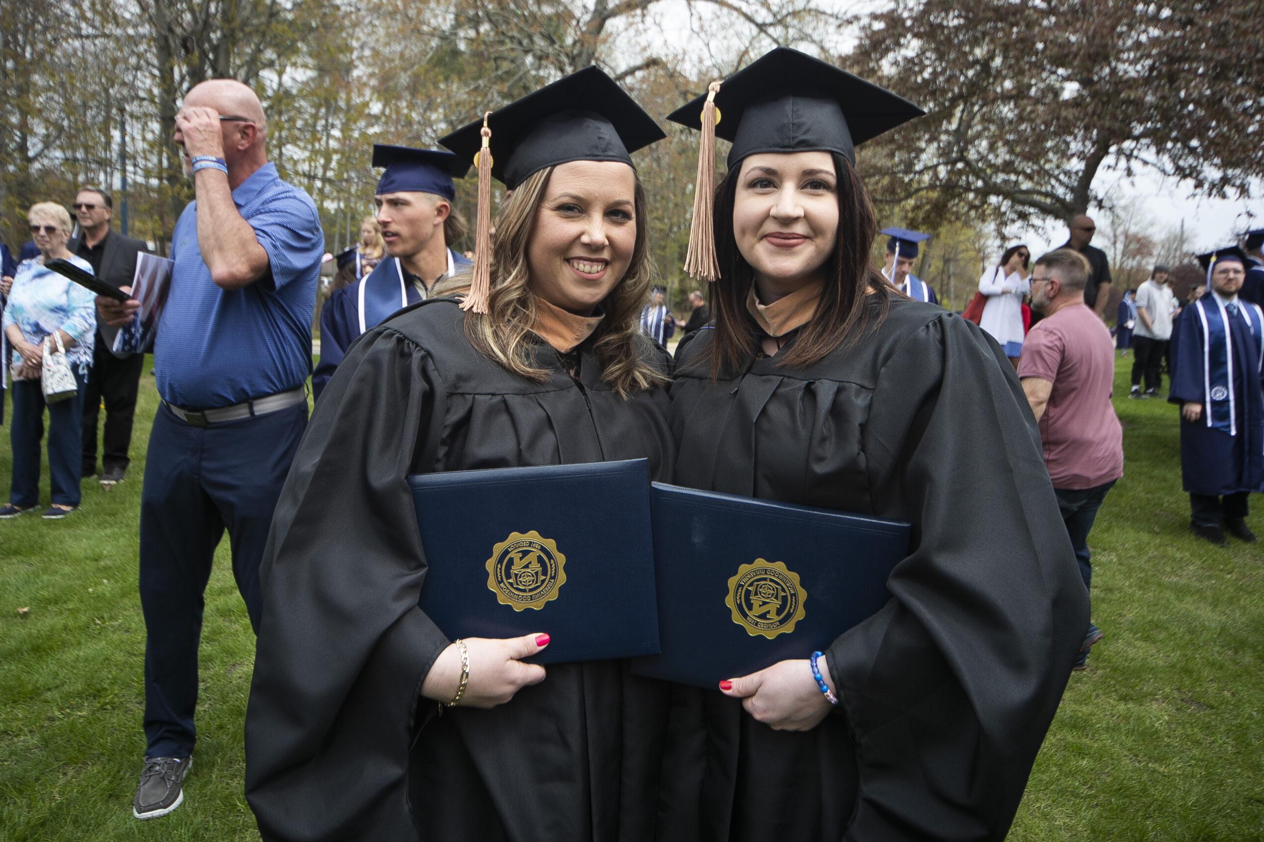 Two Northwood graduates in cap and gown holding up their diplomas outside